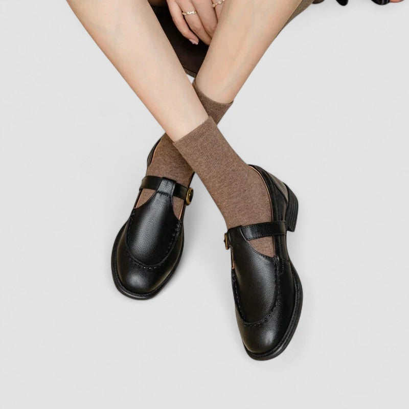 Black leather square toe Mary Jane shoes with ankle strap and brown socks — front angled view