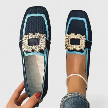 Navy blue loafers with light blue trim and crystal square buckle — hand holding shoe next to foot wearing pair