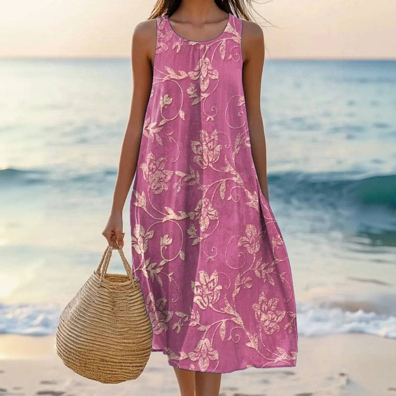 Women's pink floral maxi dress with tan woven bag on beach — front view