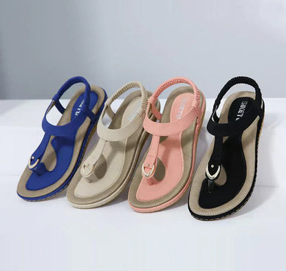 Four pairs of T-strap flat sandals with elastic slingback in blue, beige, pink, and black — front angled view