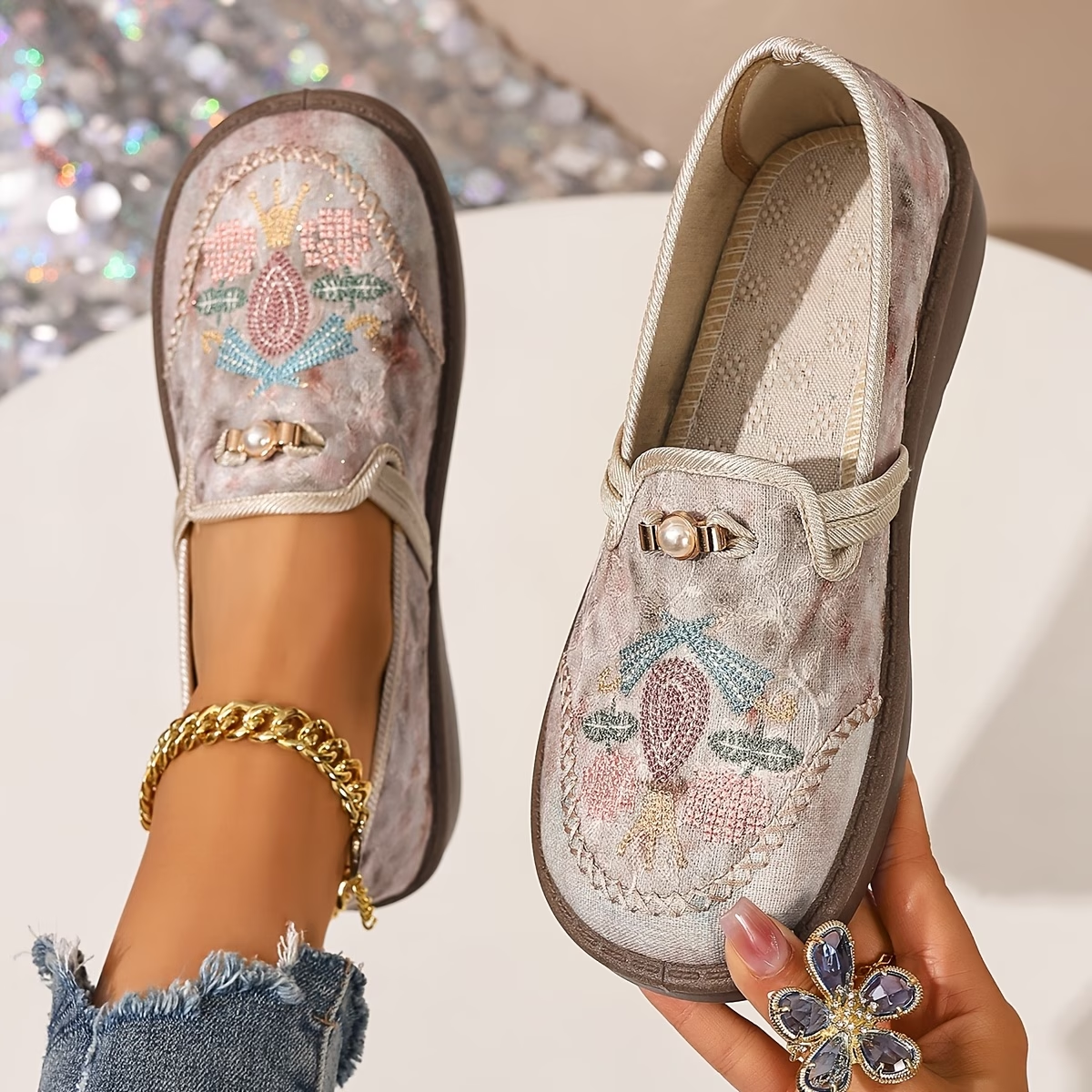 Embroidered floral loafers with pearl detail held in hand — angled product view with worn shoe visible