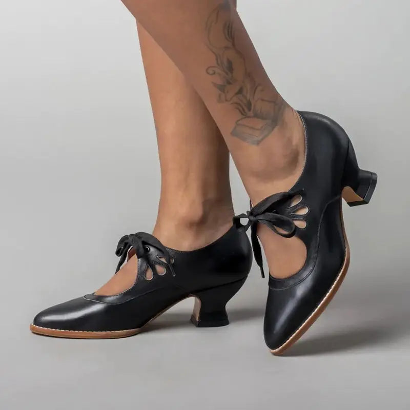 Black lace-up heeled shoes with cutout details and floral ankle tattoo — side view