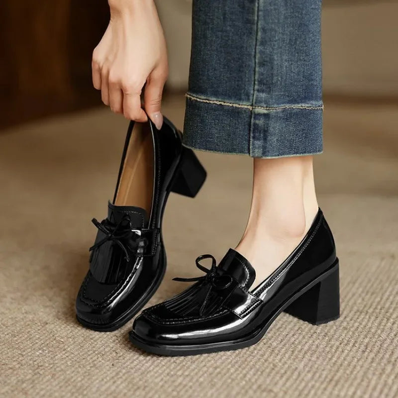 Black patent leather tassel loafer pumps with block heels on model — front three-quarter view