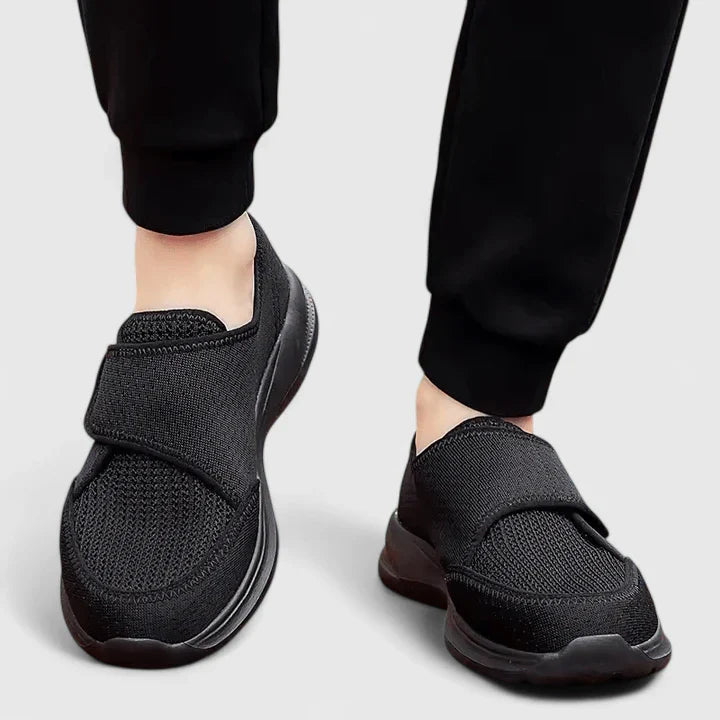 Black orthopedic comfort shoes with adjustable velcro strap — front three-quarter view on model
