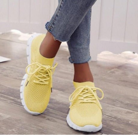 Yellow knit sock-fit sneakers with white soles on model wearing jeans — side angle view