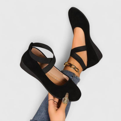 Black suede orthopedic flats with crisscross elastic straps — angled view on feet with jeans