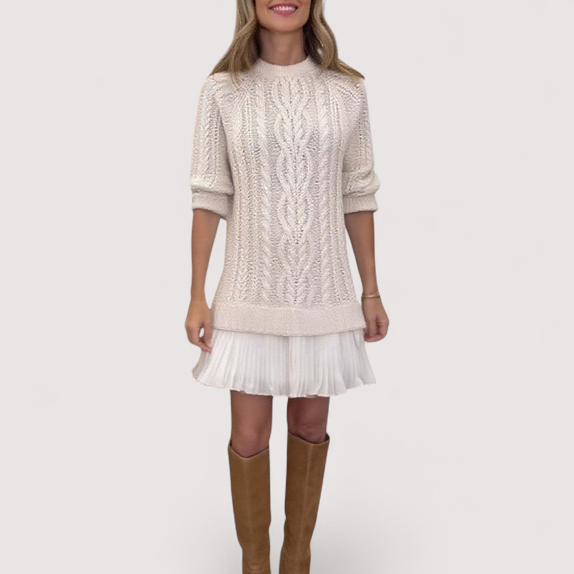 Cream cable knit sweater layered over white pleated midi dress with brown boots — front view