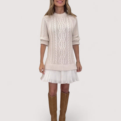 Cream cable knit sweater layered over white pleated midi dress with brown boots — front view