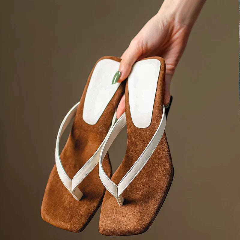 Women's brown suede wedge sandals with white straps held by hand — angled view