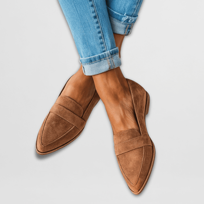 Brown suede loafers with strap detail on feet wearing cuffed jeans — angled front view