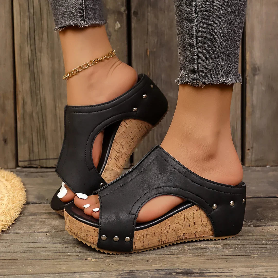 Black studded cork wedge sandals with cutout design — side view on wooden background