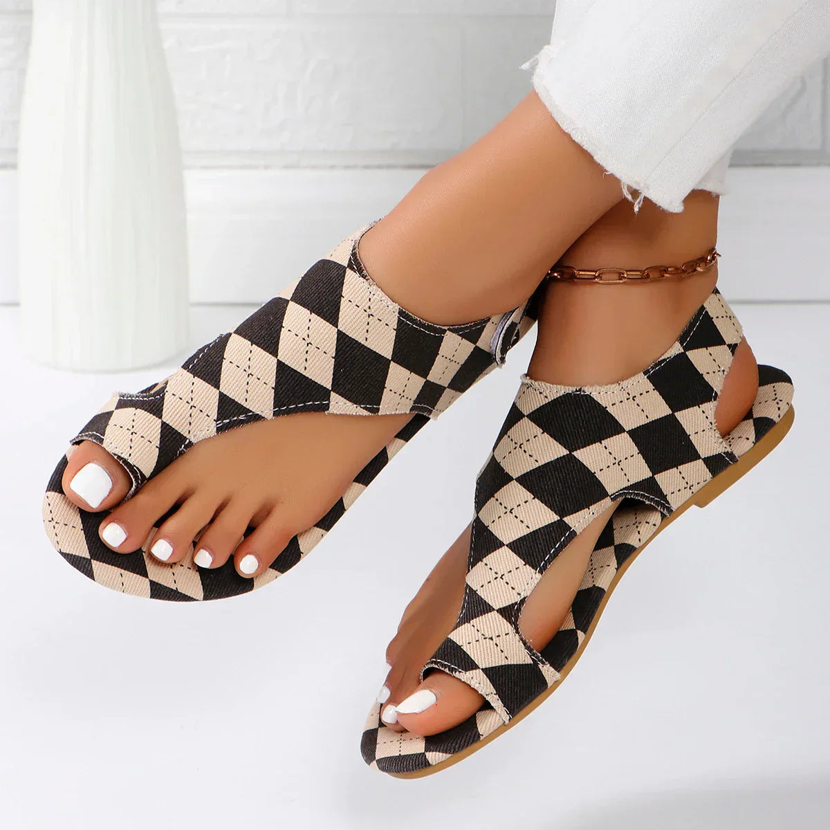 Black and beige checkered slip-on flat sandals with crisscross straps — top angled view