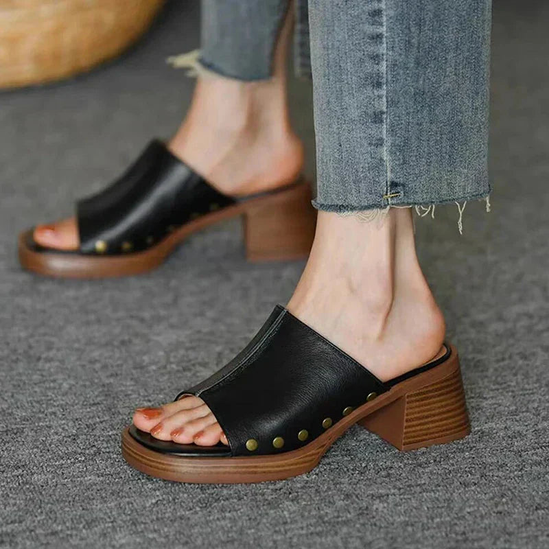 Black leather slide mule sandals with wooden block heel and studded details — angled front view