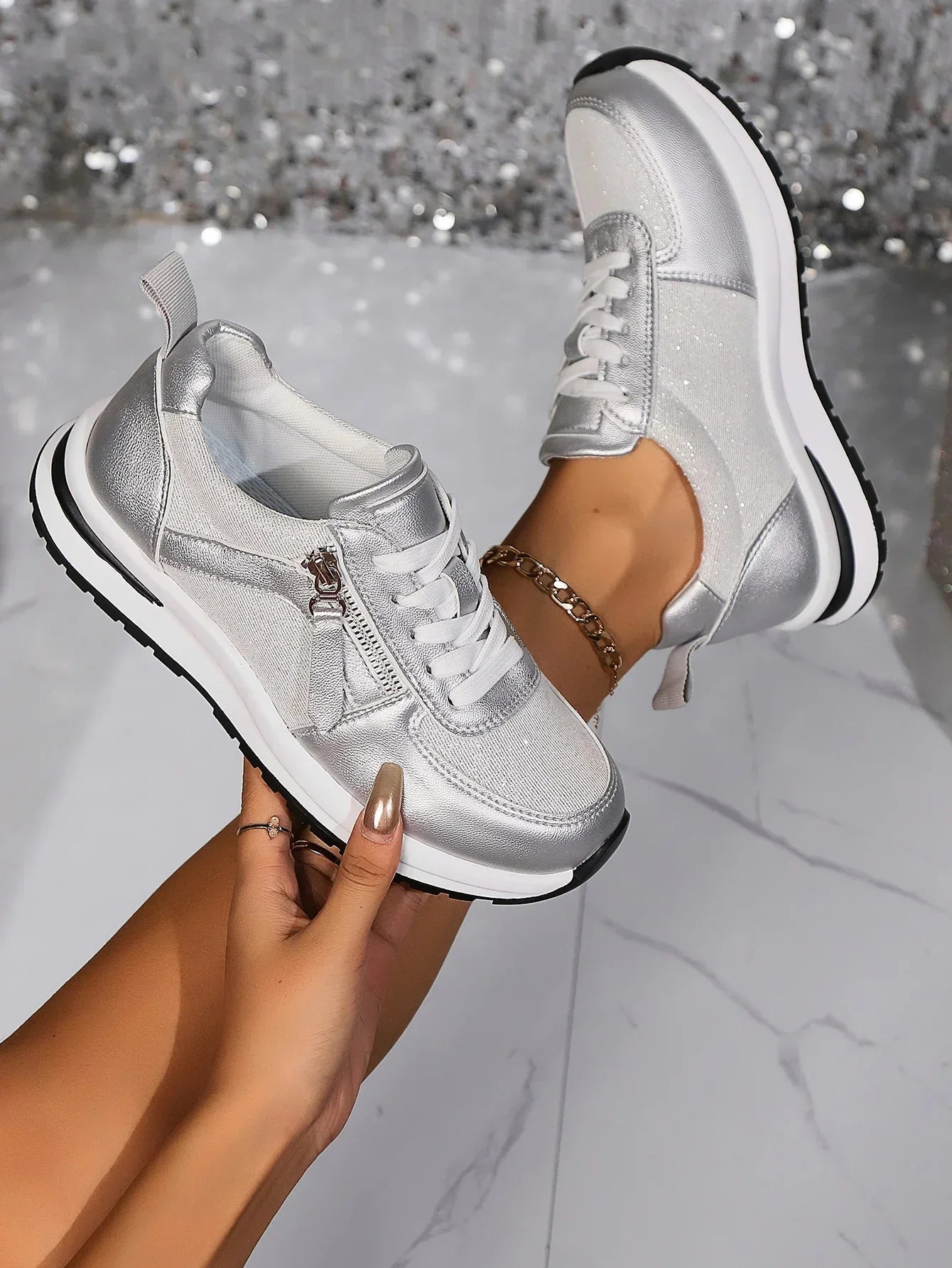 Silver platform lace-up sneakers with side zipper detail — angled view with model wearing and holding shoe
