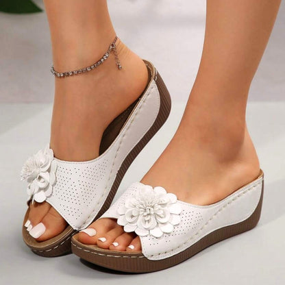 White leather wedge slides with floral decoration and perforated details — three-quarter front view on model