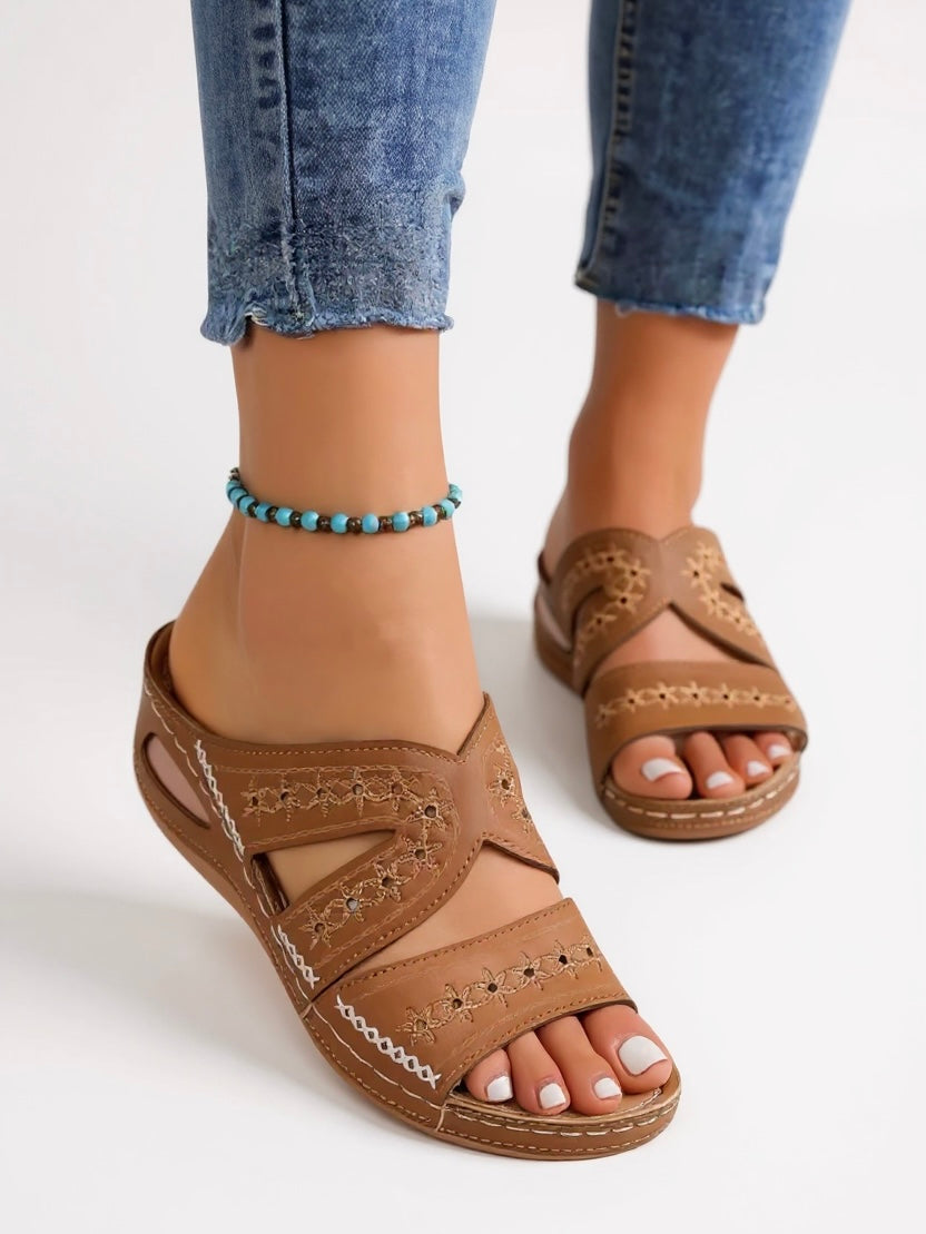 Women's tan leather slip-on flat sandals with decorative perforated straps — front angled view