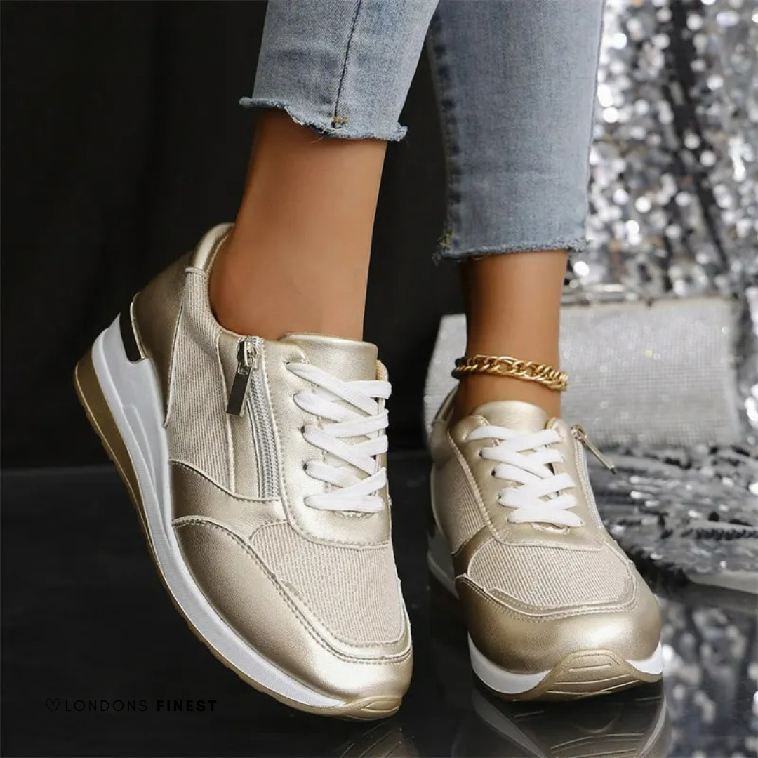 Gold metallic sneakers with white laces and side zipper on model wearing jeans — front angled view