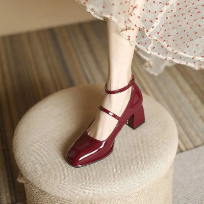 Women's burgundy patent leather square-toe Mary Jane pumps with ankle strap — side view on ottoman