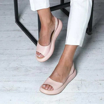 Women's pink peep-toe slingback flat sandals with open toe design — worn on model, angled front view