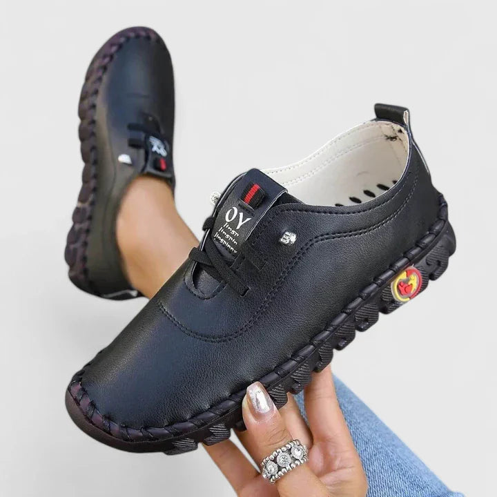 Black leather orthopedic slip-on shoes with branded label and textured sole — side view held in hand