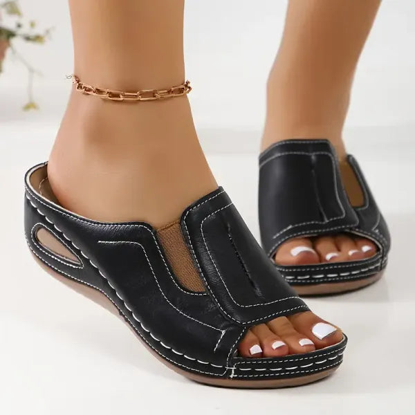 Black orthopedic slip-on sandals with white contrast stitching and arch support — front angled view on feet