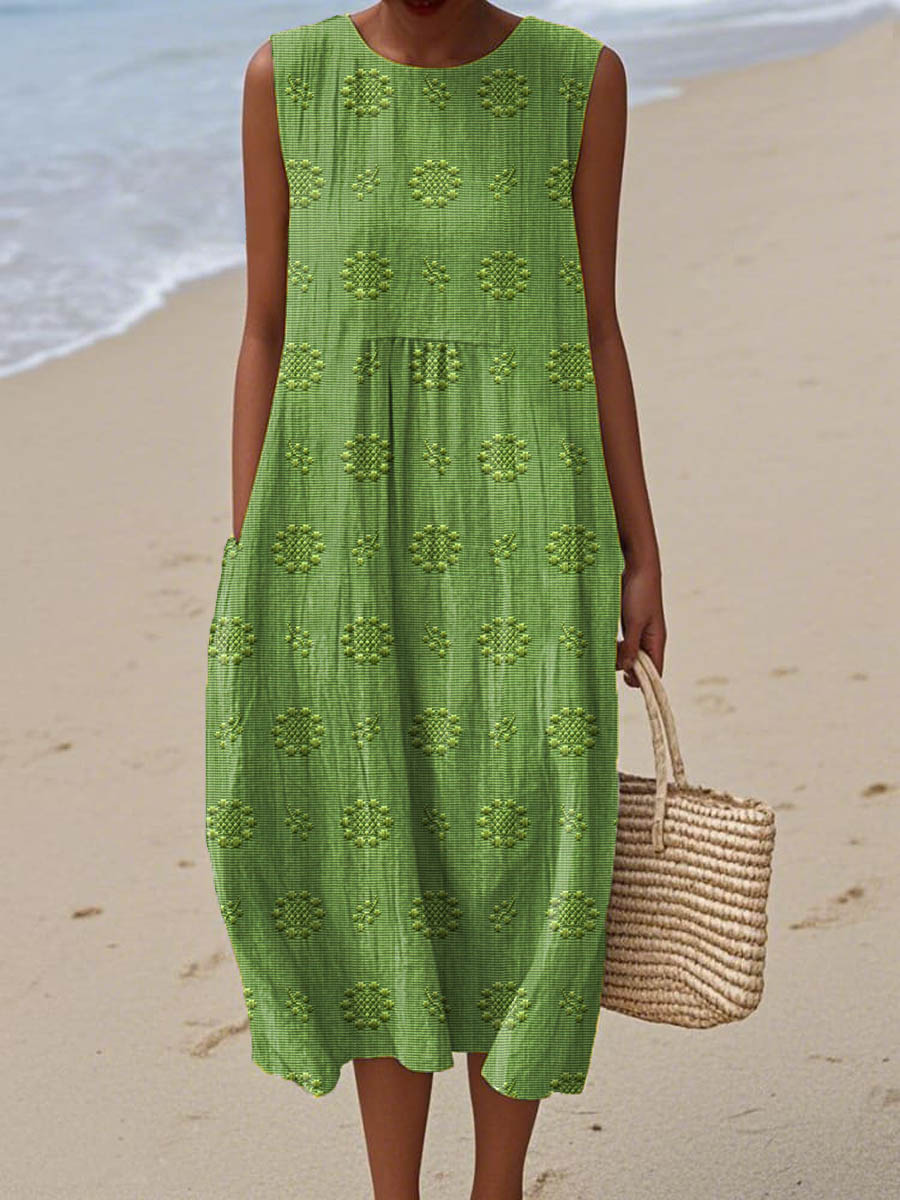 Green sleeveless midi dress with geometric embroidered pattern — front view on beach