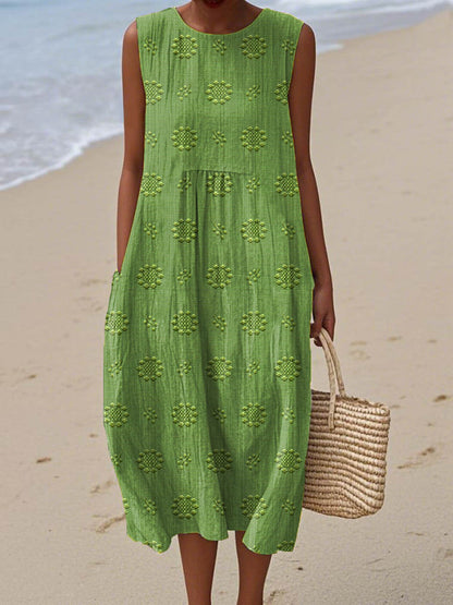 Green sleeveless midi dress with geometric embroidered pattern — front view on beach