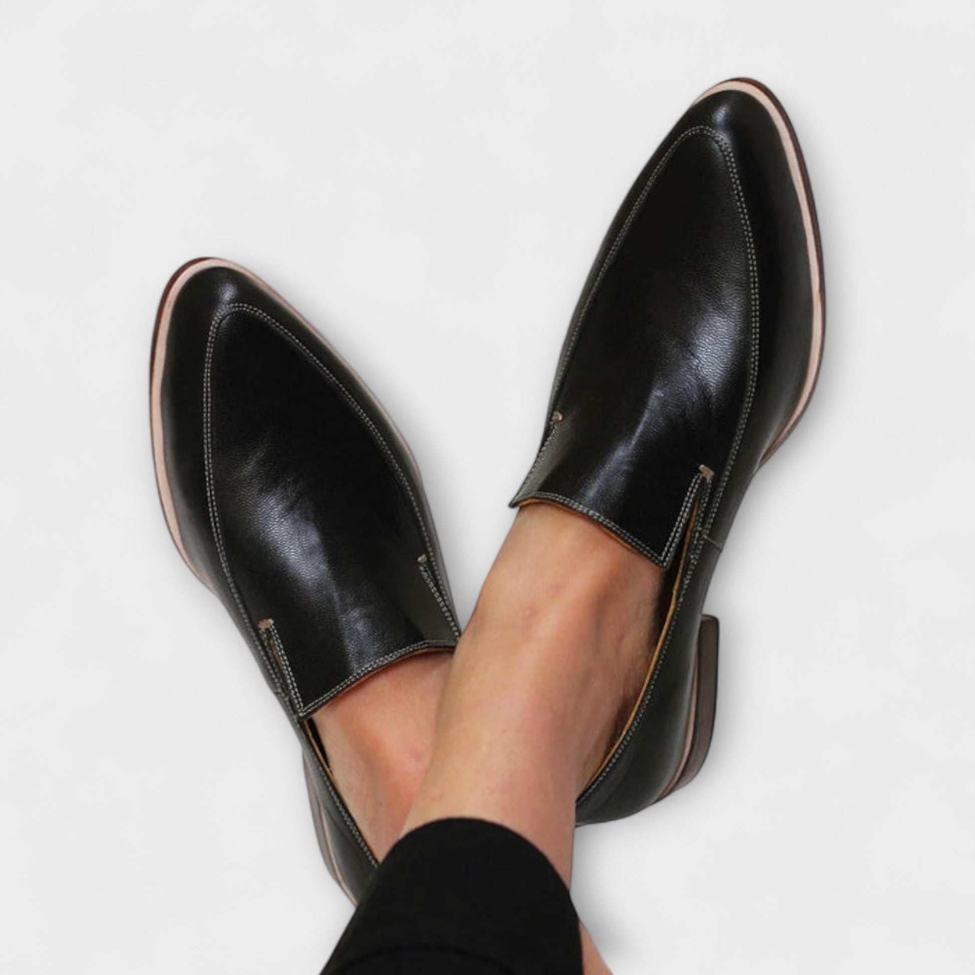 Black leather pointed-toe slip-on loafers with contrast stitching — overhead view on feet