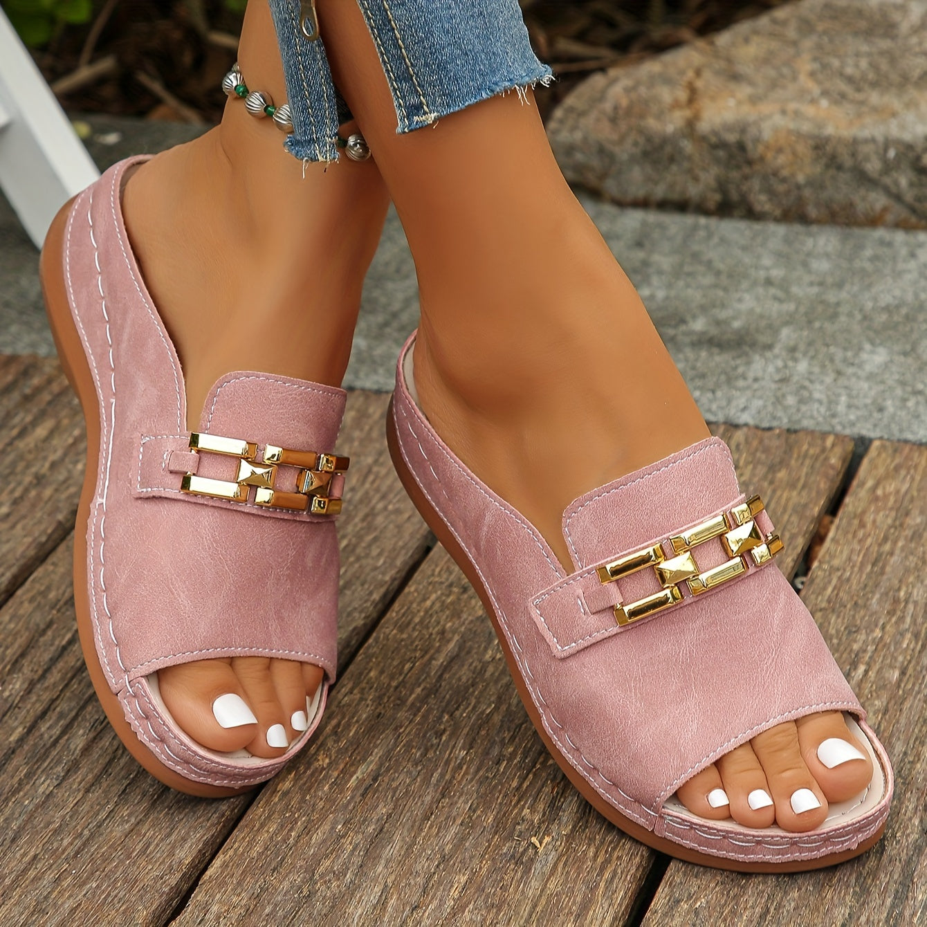 Pink cushioned flat sandals with gold chain detail on strap — angled front view on wooden deck