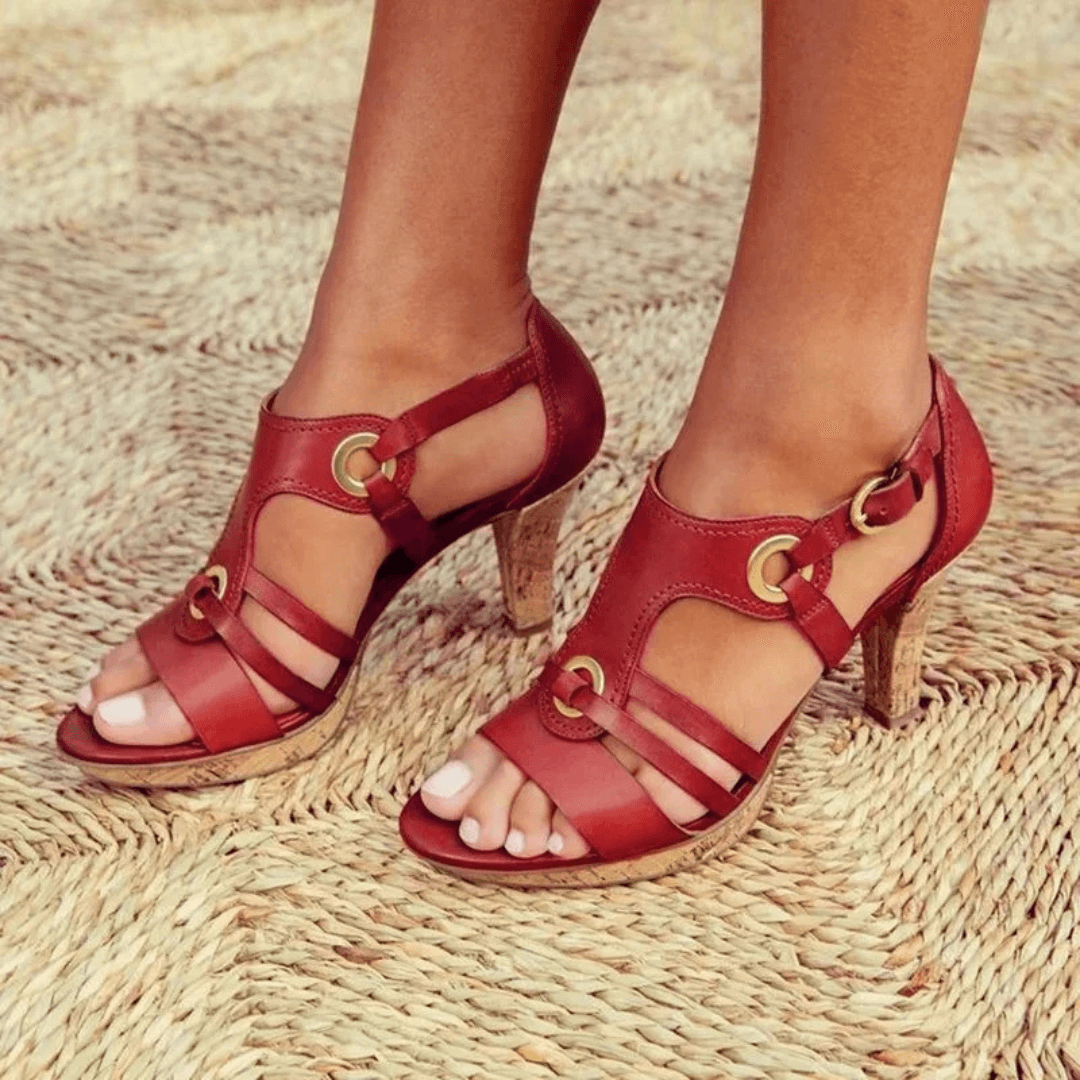 Red leather strappy sandals with gold buckle details and cork heels — front angled view on feet