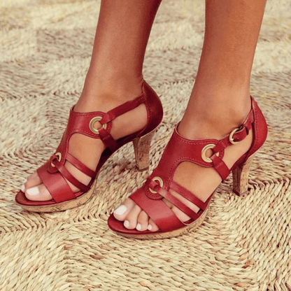 Red leather strappy sandals with gold buckle details and cork heels — front angled view on feet
